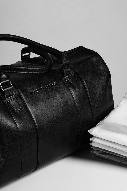 Black leather travel bag with folded shirts.